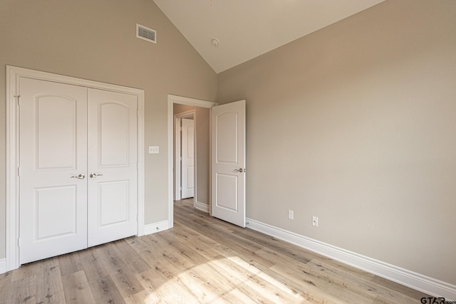 unfurnished bedroom with high vaulted ceiling, light wood-type flooring, and a closet