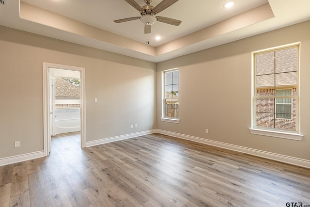 empty room featuring a raised ceiling, ceiling fan, and light hardwood / wood-style floors