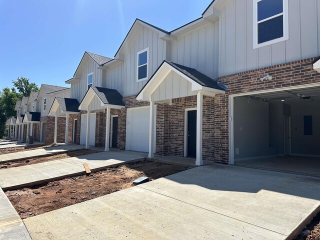 view of front of home featuring a garage, brick siding, board and batten siding, and driveway