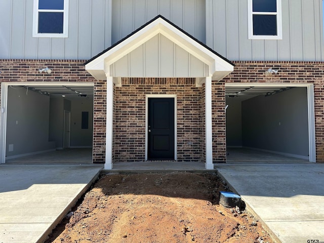 property entrance featuring driveway, a garage, board and batten siding, and brick siding