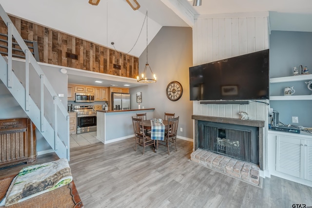 living room featuring ceiling fan with notable chandelier, a fireplace, light hardwood / wood-style floors, built in features, and high vaulted ceiling