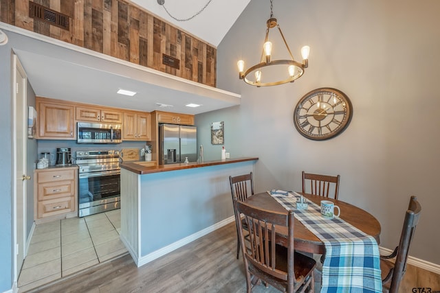 kitchen with a towering ceiling, an inviting chandelier, hanging light fixtures, appliances with stainless steel finishes, and light tile patterned floors