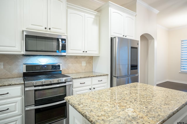 kitchen with white cabinets, ornamental molding, appliances with stainless steel finishes, tasteful backsplash, and light stone counters