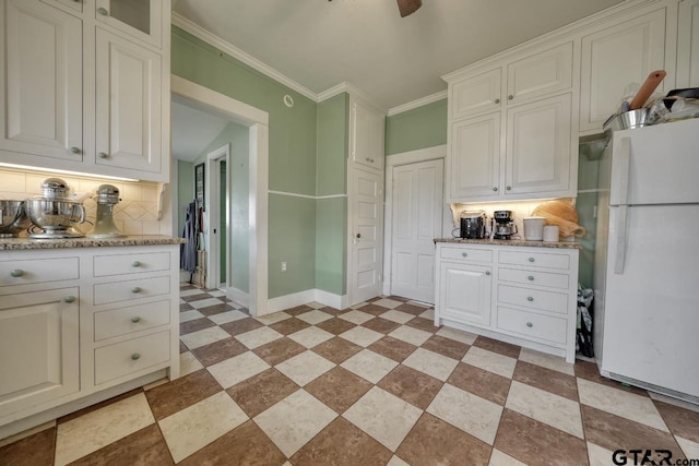 kitchen with light stone counters, decorative backsplash, white refrigerator, ornamental molding, and white cabinetry