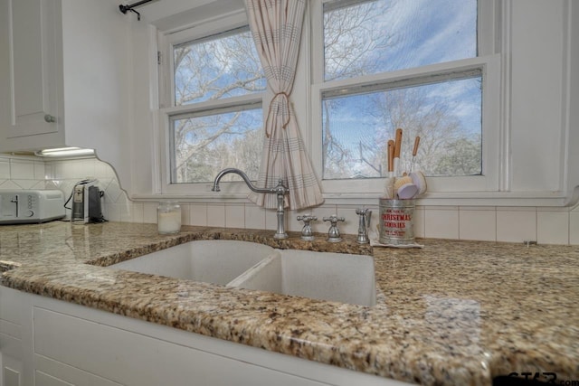 kitchen with white cabinets, sink, backsplash, and light stone countertops