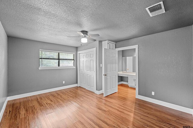 unfurnished bedroom with ceiling fan, a textured ceiling, a closet, and light hardwood / wood-style flooring