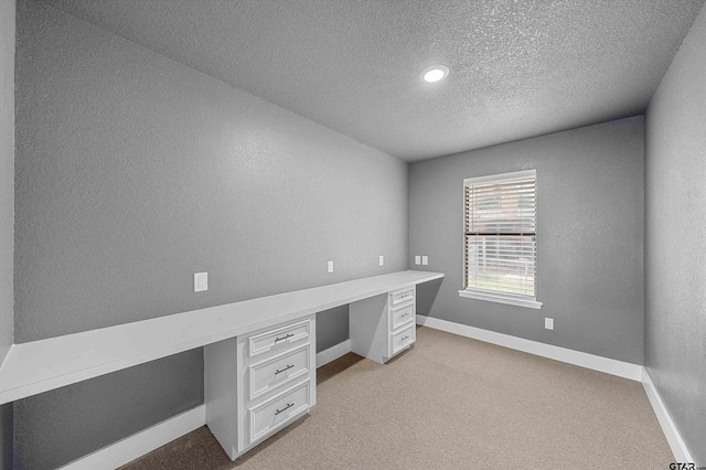 unfurnished office featuring a textured ceiling, light colored carpet, and built in desk