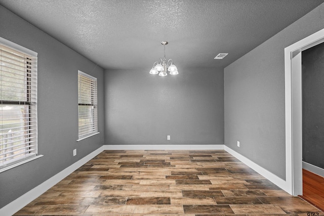 unfurnished dining area featuring dark wood-type flooring, a textured ceiling, and a notable chandelier