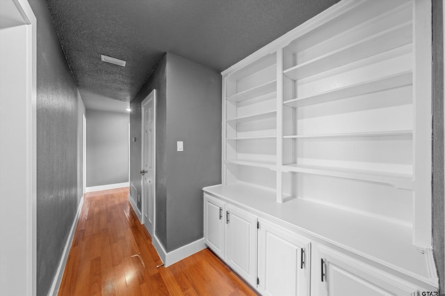 corridor with a textured ceiling and light hardwood / wood-style flooring