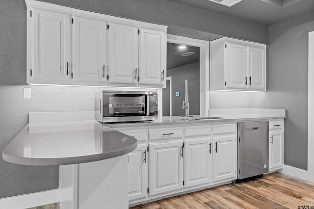 kitchen featuring stainless steel dishwasher, white cabinetry, sink, and light wood-type flooring