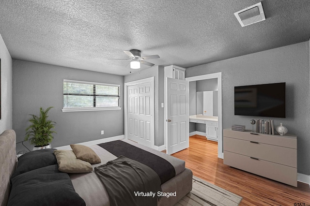 bedroom with a closet, ensuite bath, light wood-type flooring, a textured ceiling, and ceiling fan