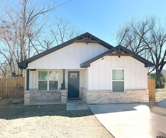 view of front facade with stone siding, a porch, board and batten siding, and fence