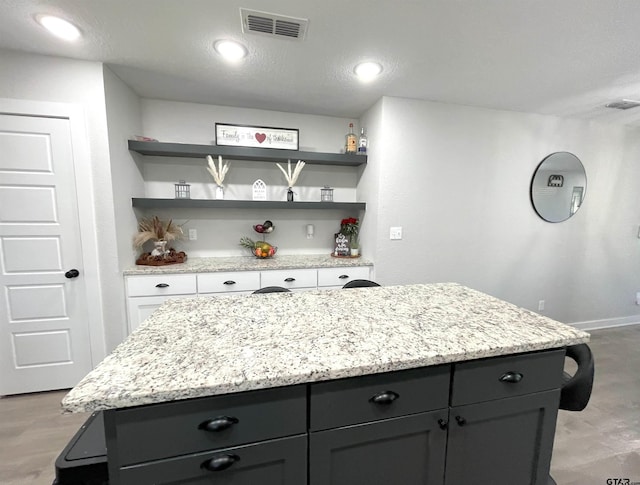 kitchen featuring light stone counters, a center island, visible vents, and open shelves