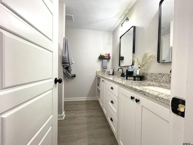 full bathroom with a sink, wood finished floors, visible vents, baseboards, and double vanity