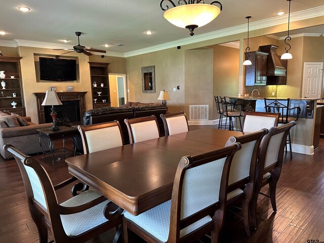 dining area featuring visible vents, crown molding, a fireplace, dark wood-style floors, and a ceiling fan