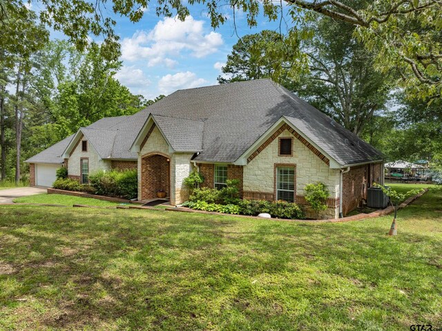 view of front of home featuring a front lawn, stone siding, roof with shingles, brick siding, and central AC unit