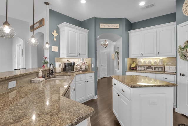 kitchen with pendant lighting, white cabinets, sink, stone countertops, and kitchen peninsula