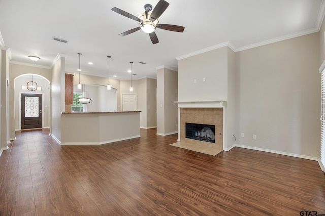 unfurnished living room with dark wood-style flooring, ceiling fan, ornamental molding, and a tile fireplace