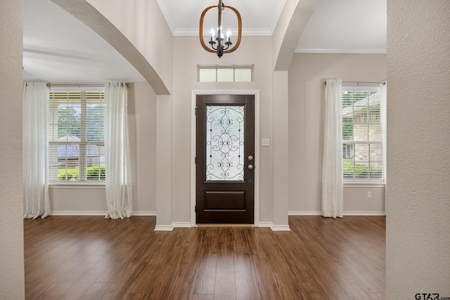 foyer with an inviting chandelier, arched walkways, baseboards, wood finished floors, and ornamental molding