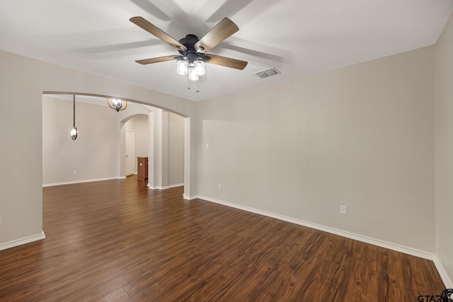 spare room with visible vents, arched walkways, dark wood-type flooring, and a ceiling fan