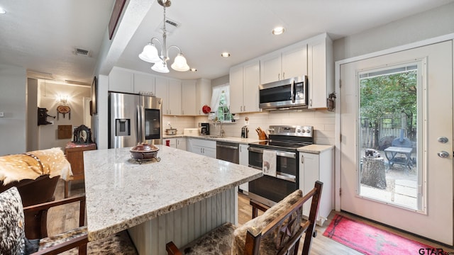 kitchen featuring stainless steel appliances, white cabinets, a kitchen island, light wood-type flooring, and decorative light fixtures