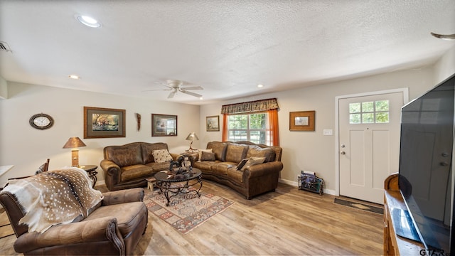 living room featuring a textured ceiling, light wood-type flooring, and ceiling fan