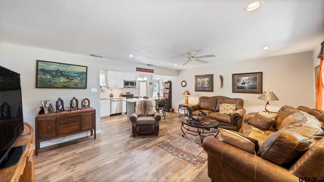 living room featuring a textured ceiling, light wood-type flooring, and ceiling fan