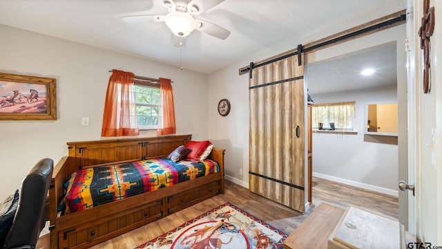 bedroom with hardwood / wood-style flooring, a barn door, and ceiling fan