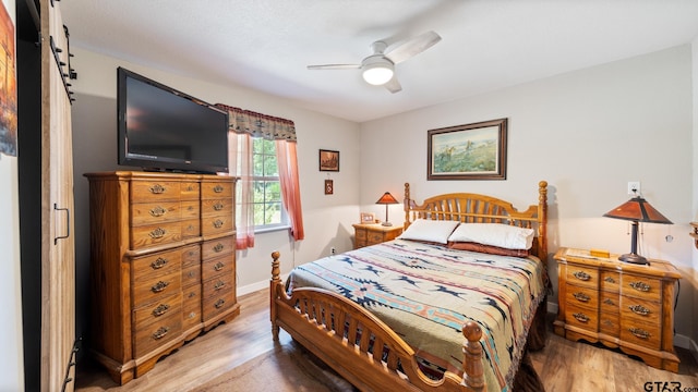 bedroom featuring hardwood / wood-style floors, ceiling fan, and a barn door