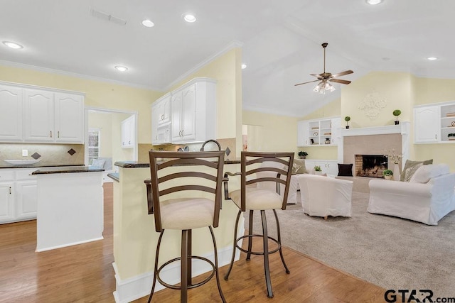 kitchen featuring a breakfast bar, dark countertops, white cabinets, light wood-style floors, and ceiling fan