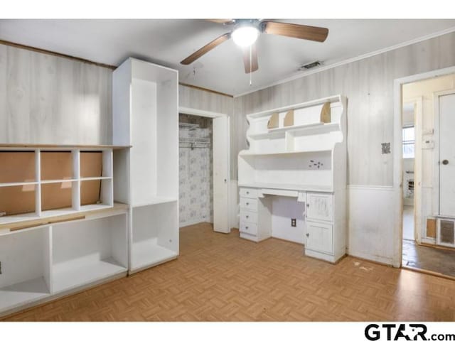 unfurnished office featuring parquet flooring, a ceiling fan, visible vents, built in desk, and crown molding