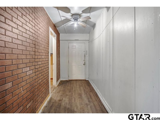 hall featuring brick wall, baseboards, and wood finished floors