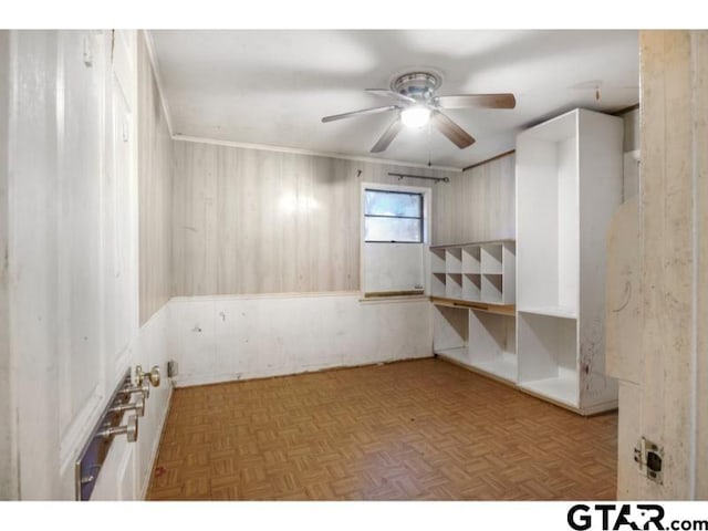 spare room with ornamental molding, a ceiling fan, and wooden walls