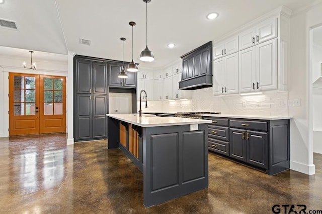 kitchen with a kitchen island with sink, sink, white cabinets, and hanging light fixtures