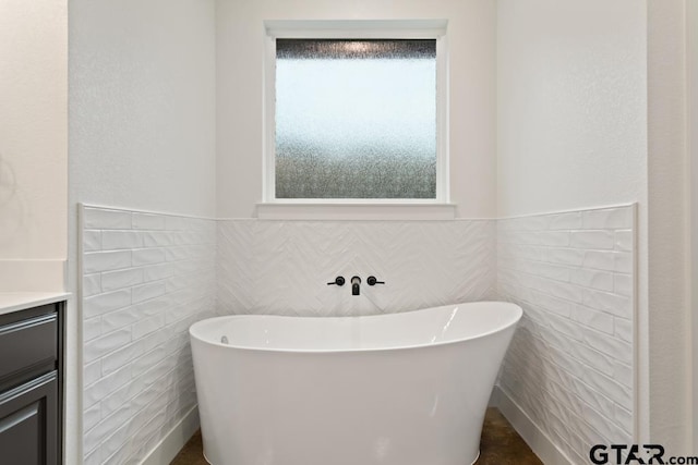 bathroom with a washtub, vanity, a healthy amount of sunlight, and tile walls