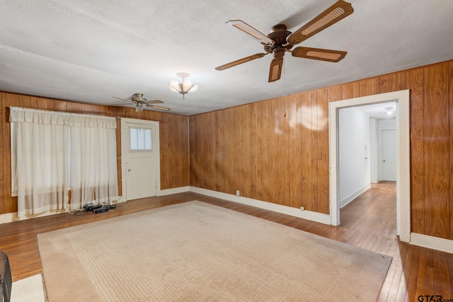 empty room featuring wood-type flooring, a textured ceiling, ceiling fan, and wood walls