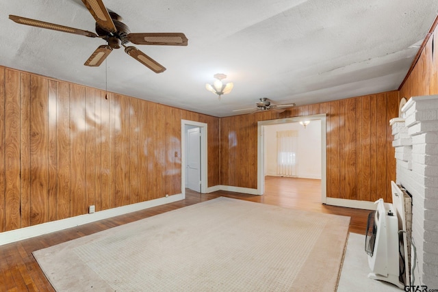 unfurnished living room featuring heating unit, wood walls, wood-type flooring, and a textured ceiling