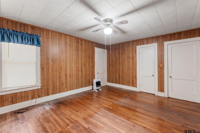 unfurnished room with heating unit, wood walls, ceiling fan, and wood-type flooring