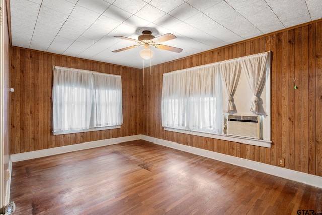 spare room featuring hardwood / wood-style floors, a healthy amount of sunlight, wooden walls, and cooling unit