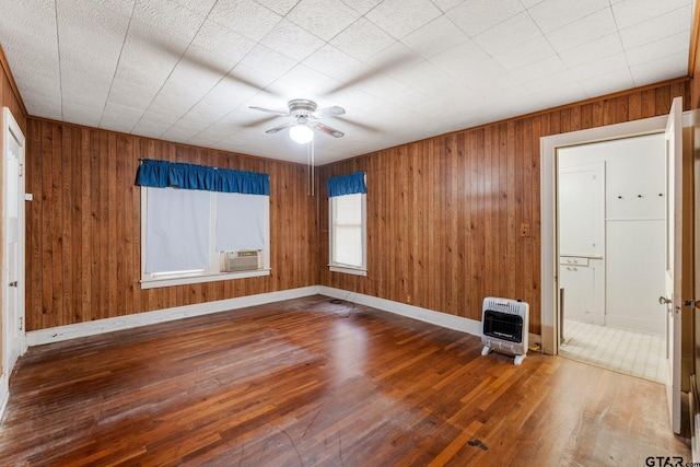 empty room featuring heating unit, cooling unit, ceiling fan, wooden walls, and wood-type flooring