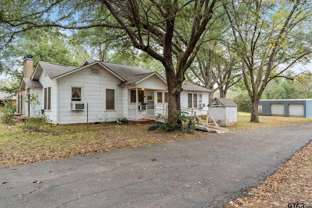 view of front of house featuring covered porch, a garage, cooling unit, and a storage shed