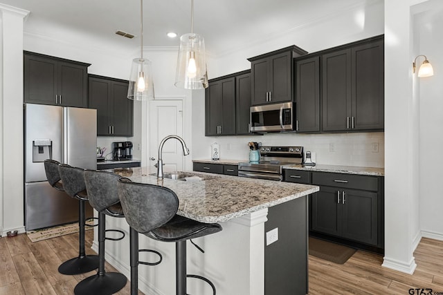 kitchen featuring wood-type flooring, appliances with stainless steel finishes, an island with sink, pendant lighting, and sink