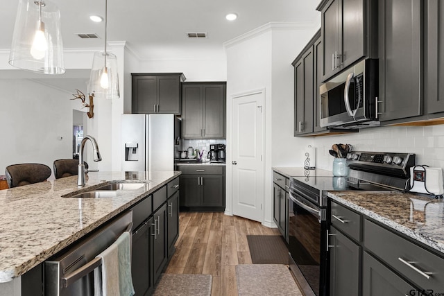 kitchen with stainless steel appliances, an island with sink, ornamental molding, dark hardwood / wood-style flooring, and sink