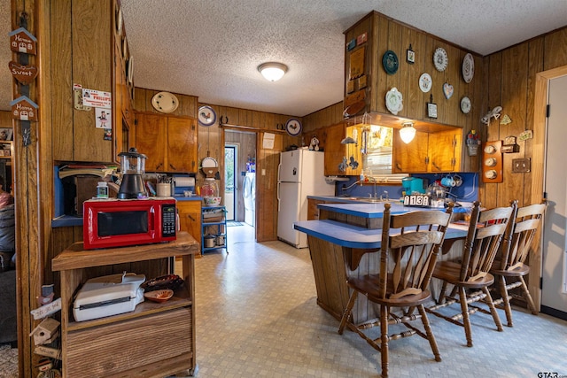 kitchen with wooden walls, a textured ceiling, sink, and white refrigerator