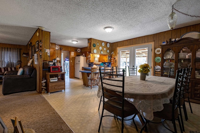 dining room with wooden walls, french doors, and a textured ceiling