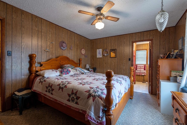 carpeted bedroom with a textured ceiling, wood walls, and ceiling fan