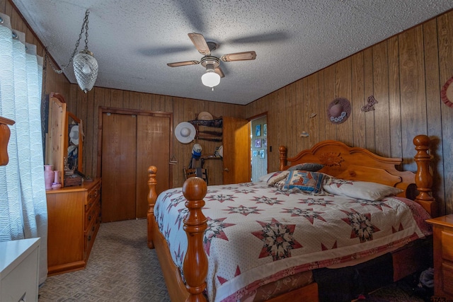 carpeted bedroom featuring a closet, wooden walls, a textured ceiling, and ceiling fan