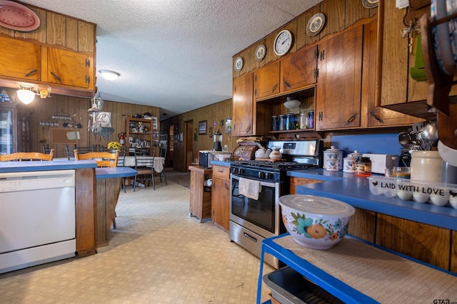 kitchen with dishwasher, wood walls, a textured ceiling, and stainless steel gas range oven