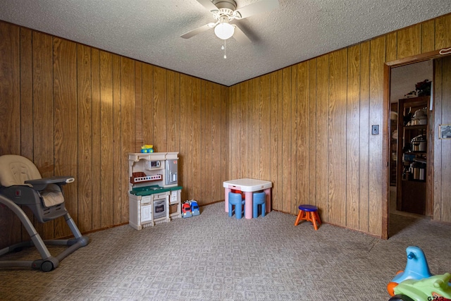 recreation room featuring a textured ceiling, wooden walls, and ceiling fan