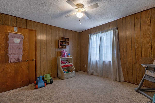 recreation room featuring a textured ceiling, light carpet, wooden walls, and ceiling fan